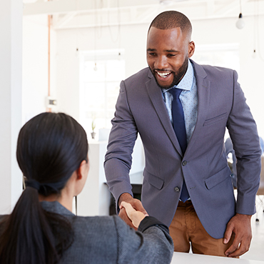 professional african american male standing up shaking the hand of a professional woman at a desk